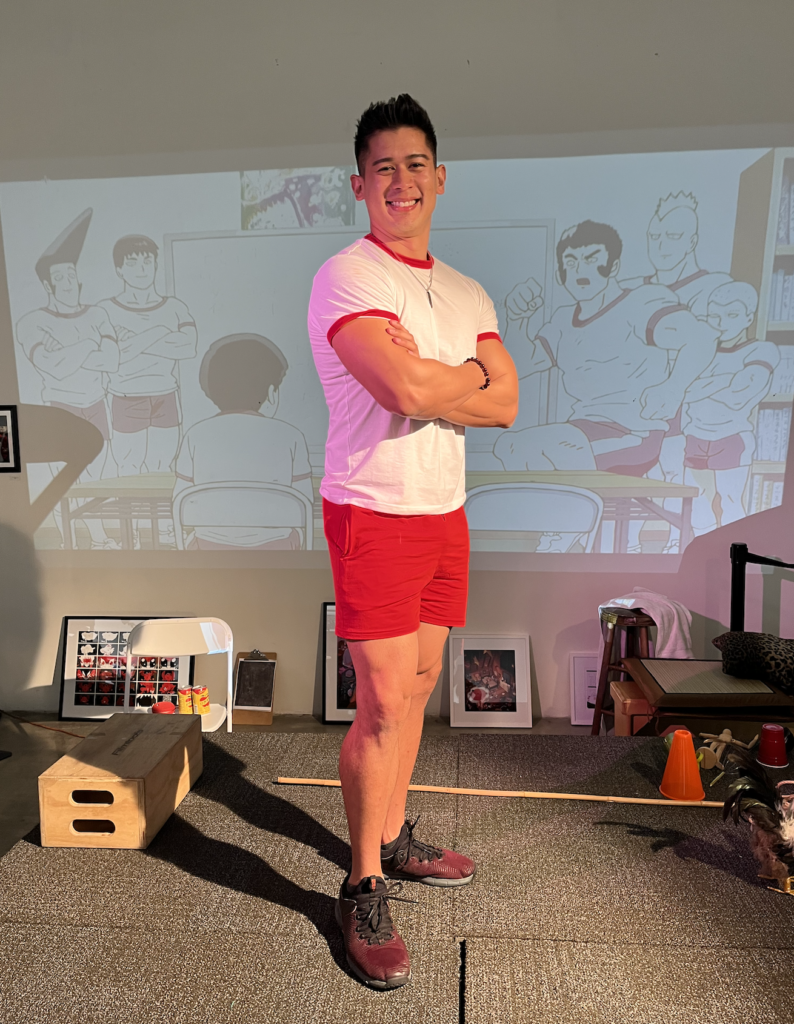 Calix Quan, smiling, arms crossed, right left forward, posing proudly. Behind him, The Body Improvement Club stands at a white board crossing their arms too, projected on the wall.